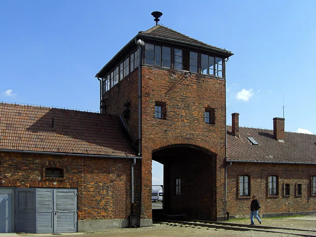 La portalada de l'edifici de guàrdia i les vies de ferrocarril que conduïen al camp d'extermini nazi d'Auschwitz II-Birkenau. Símbol tràgic del genocidi i la barbàrie industrialitzada de l'Holocaust.